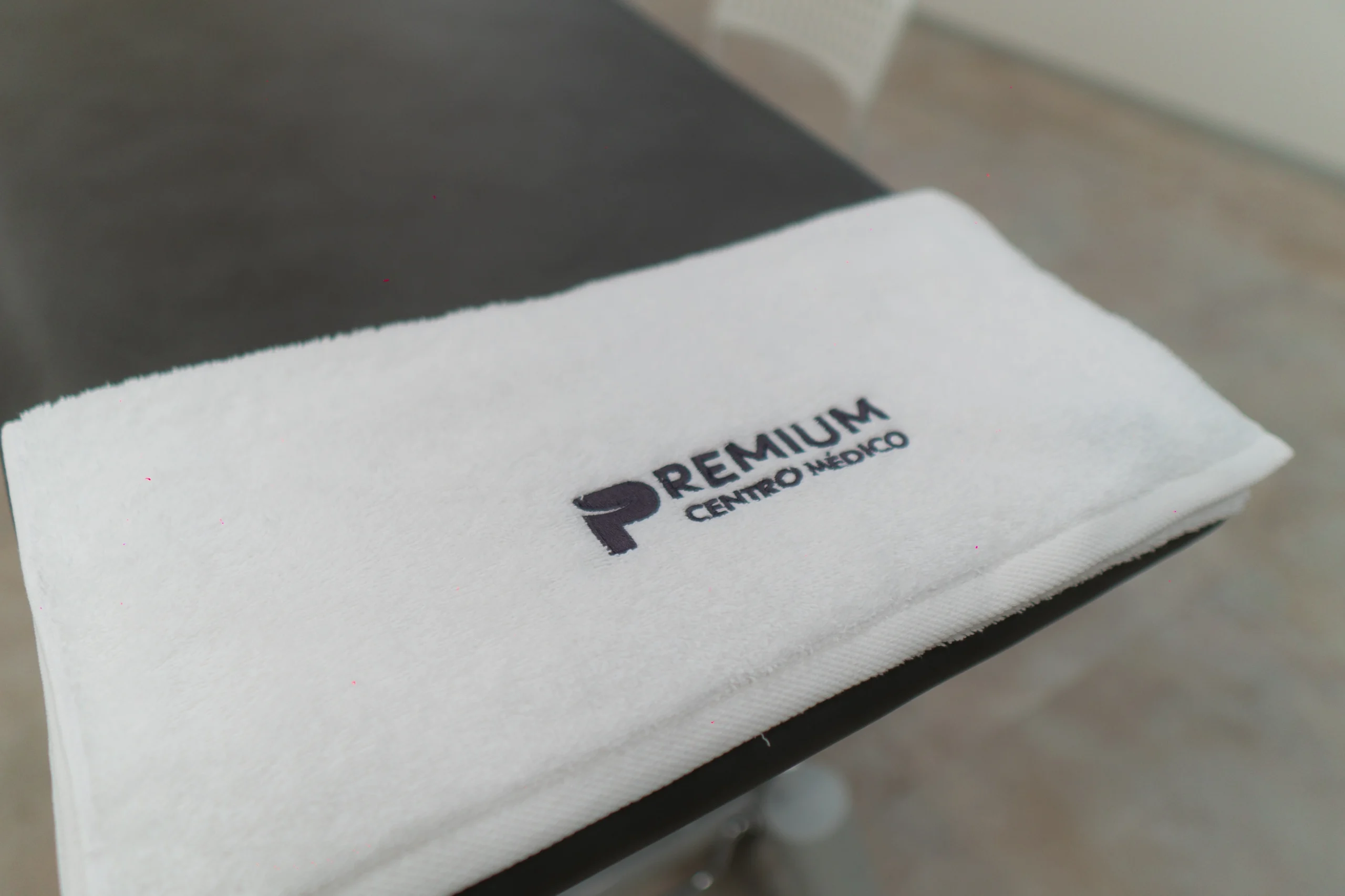 Toalla blanca bordada con el logo de Premium Centro Médico sobre una camilla de tratamiento, reflejando calidad y atención personalizada.