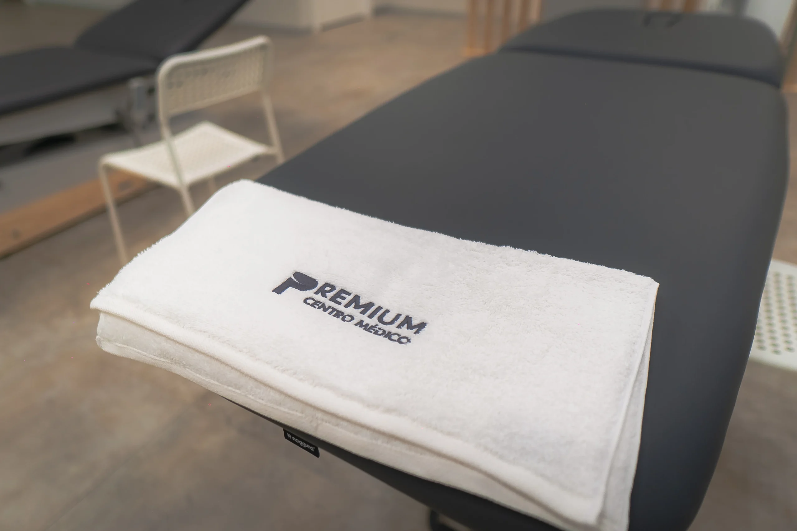 Toalla blanca bordada con el logo de Premium Centro Médico sobre una camilla de tratamiento, reflejando calidad y atención personalizada.